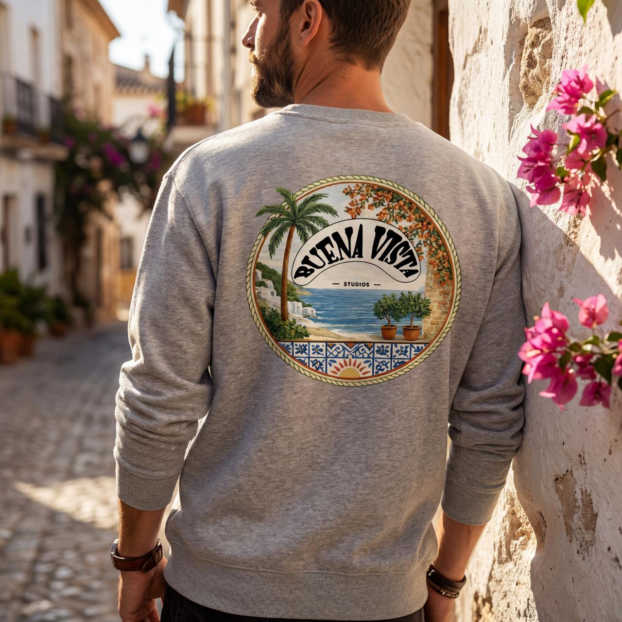 Person wearing a gray sweatshirt with a 'Buena Vista' graphic on the back, standing in a sunlit street.