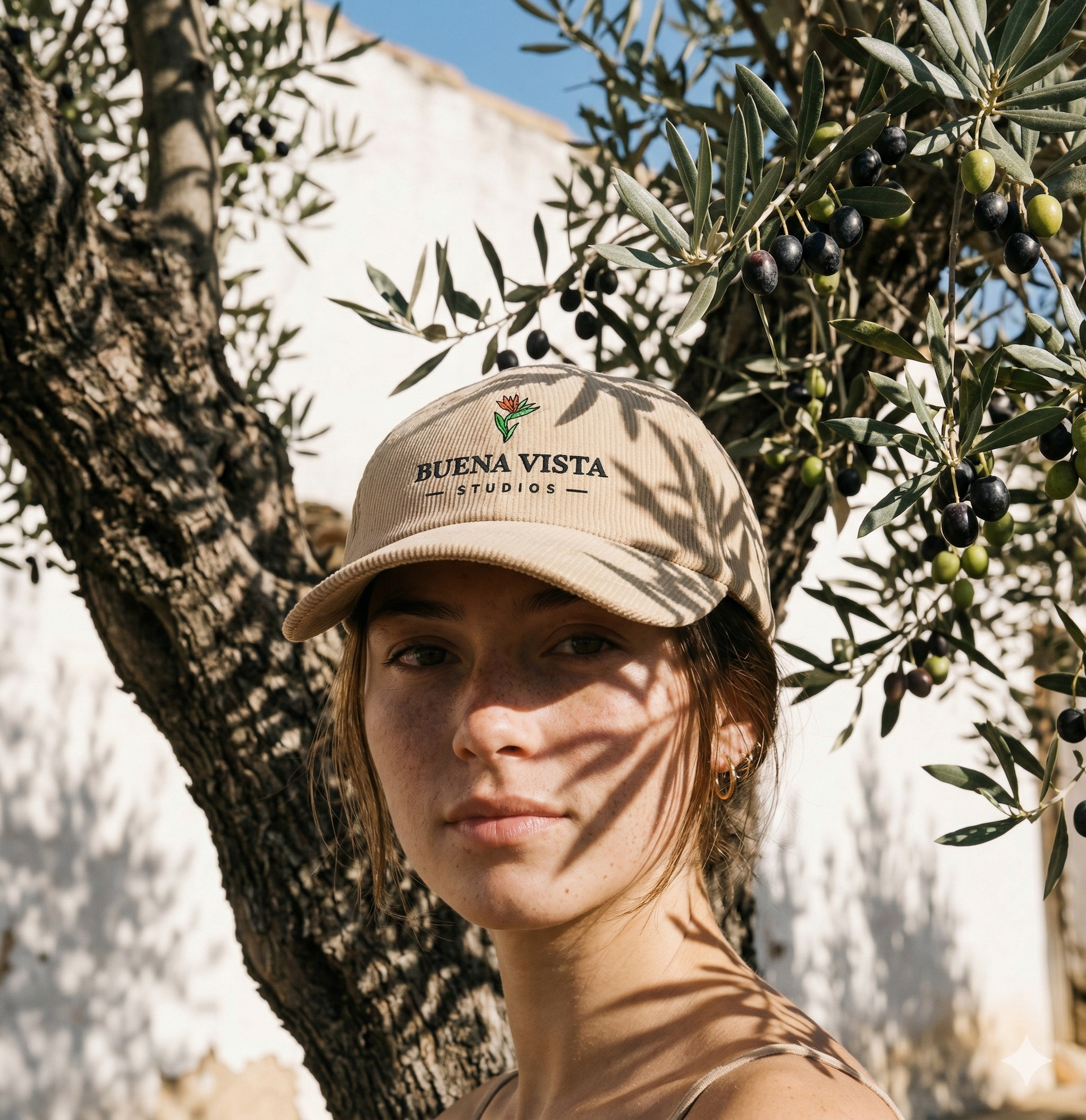 Person wearing a beige cap with 'Buena Vista Studios' logo in front of an olive tree.